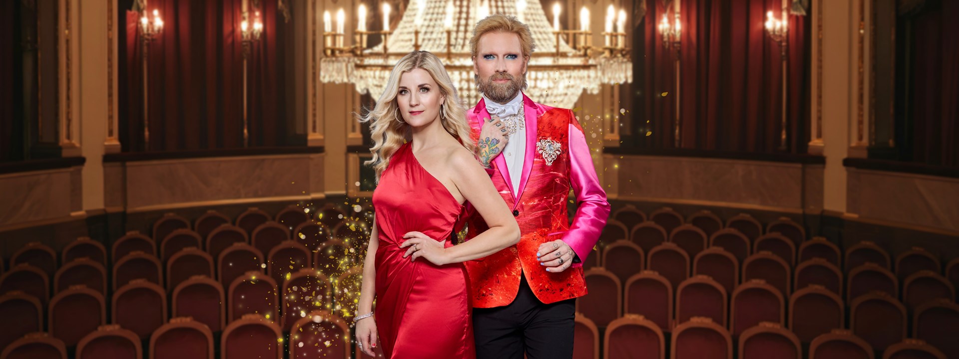 Affischbild för julkonserten En Fridfull Jul med Emmi Christensson och Rickard Söderberg. En man och en kvinna i finkläder står i en upplyst salong med kristallkrona, röda stolar och draperier.