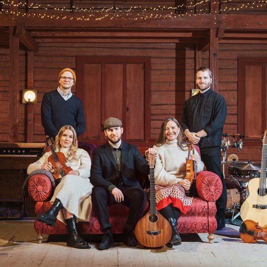 Affischbild för julkonserten och bandet "I midvintertid".  Fem musiker, tre män och två kvinnor, sitter eller står kring en soffa i rött brokadtyg. Omkring sig har de instrument som fiol, orgel, trummor, gitarr och luta. I taket hänger ljusslingor och på golvet står två stora ljusstakar med levande ljus. 