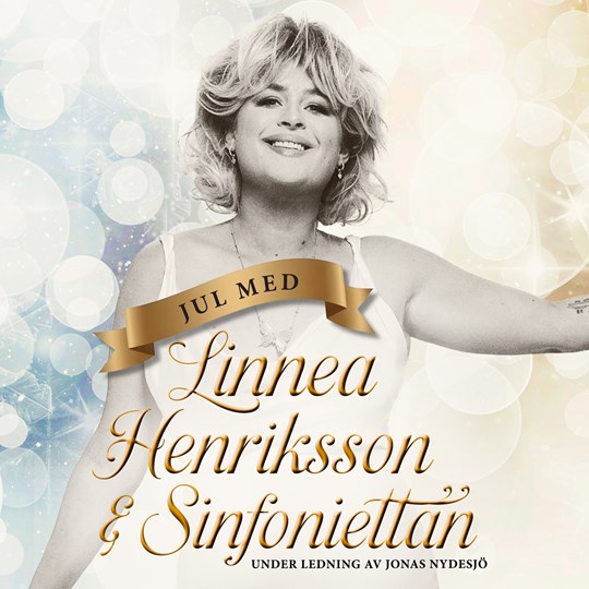 Affischbild för julkonserten "Jul med Linnea Henriksson & Sinfoniettan". En blond, leende kvinna mot en gnistrande bakgrund. 