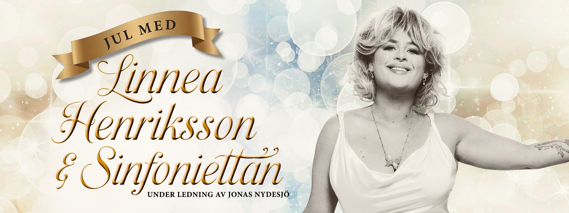 Affischbild för julkonserten "Jul med Linnea Henriksson & Sinfoniettan". En blond, leende kvinna mot en gnistrande bakgrund. 