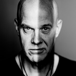 Affischbild för Questar med Jacob Karlzon. En man i svart t-shirt. Skuggor far över hans ansikte.