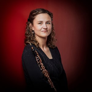 Affischbild för Jönköpings Sinfoniettas konsert Mozart och Morricone. En kvinna med en oboe framför en röd vägg.