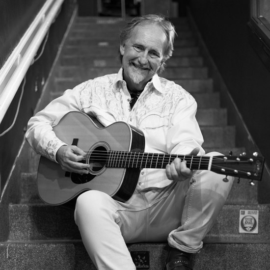 Affischbild för Drew Young. Leende man med en gitarr i famnen.