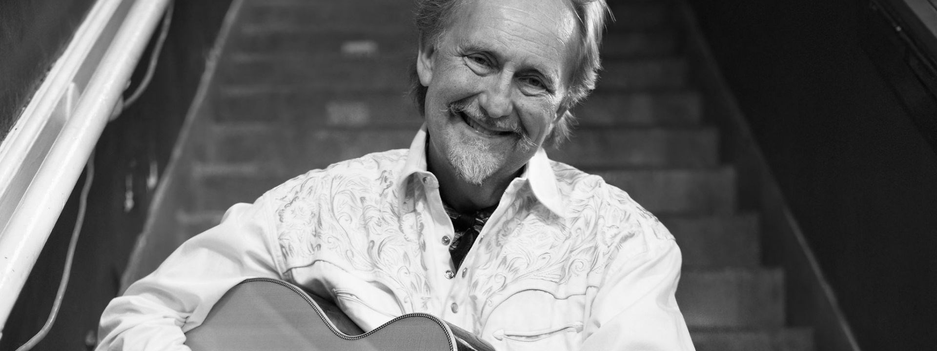 Affischbild för Drew Young. Leende man med en gitarr i famnen.